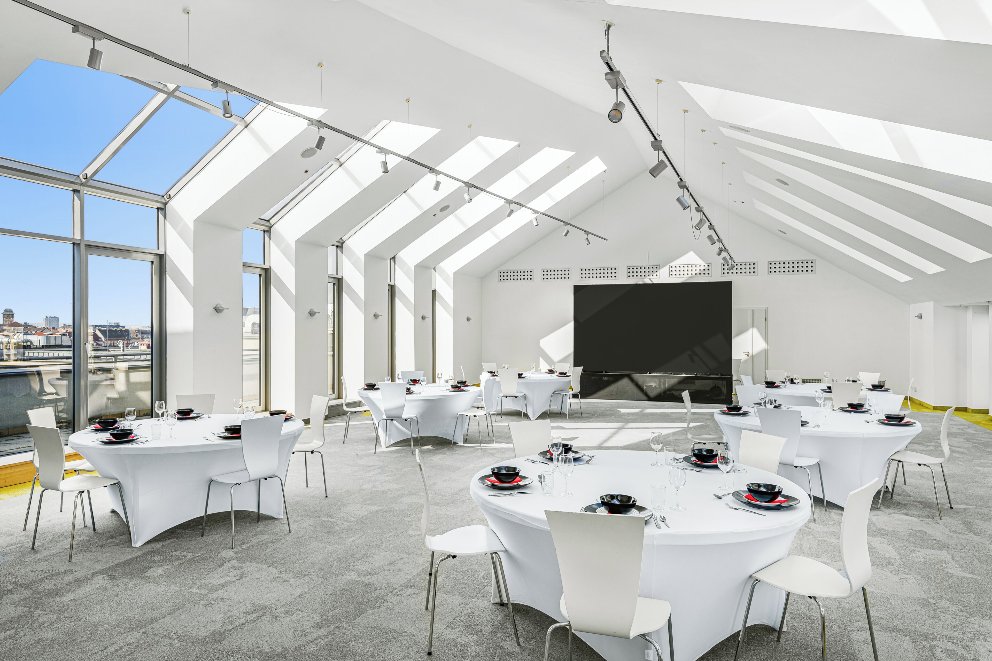 A modern conference room with white tables and chairs, large windows, and a city view.