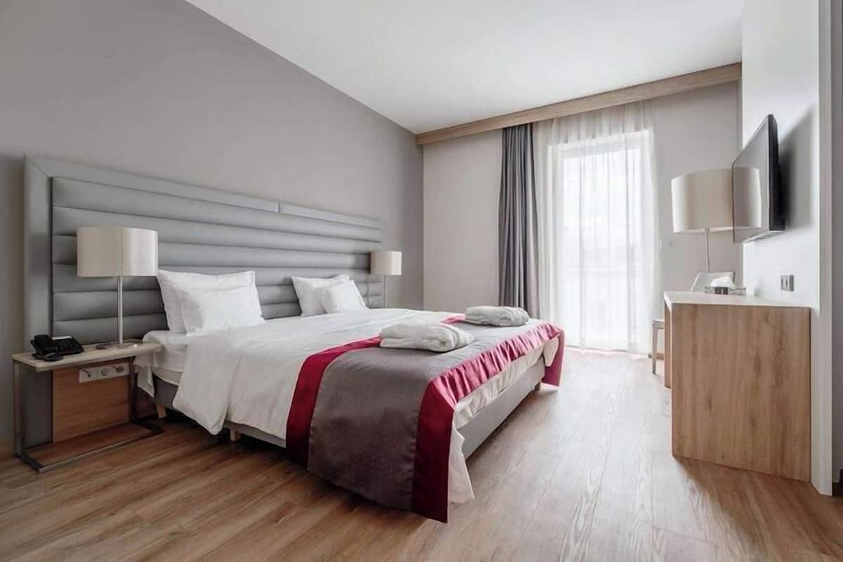 Une chambre d’hôtel moderne dotée d’un grand lit, de tables de chevet, d’un téléviseur à écran plat et d’une commode en bois.