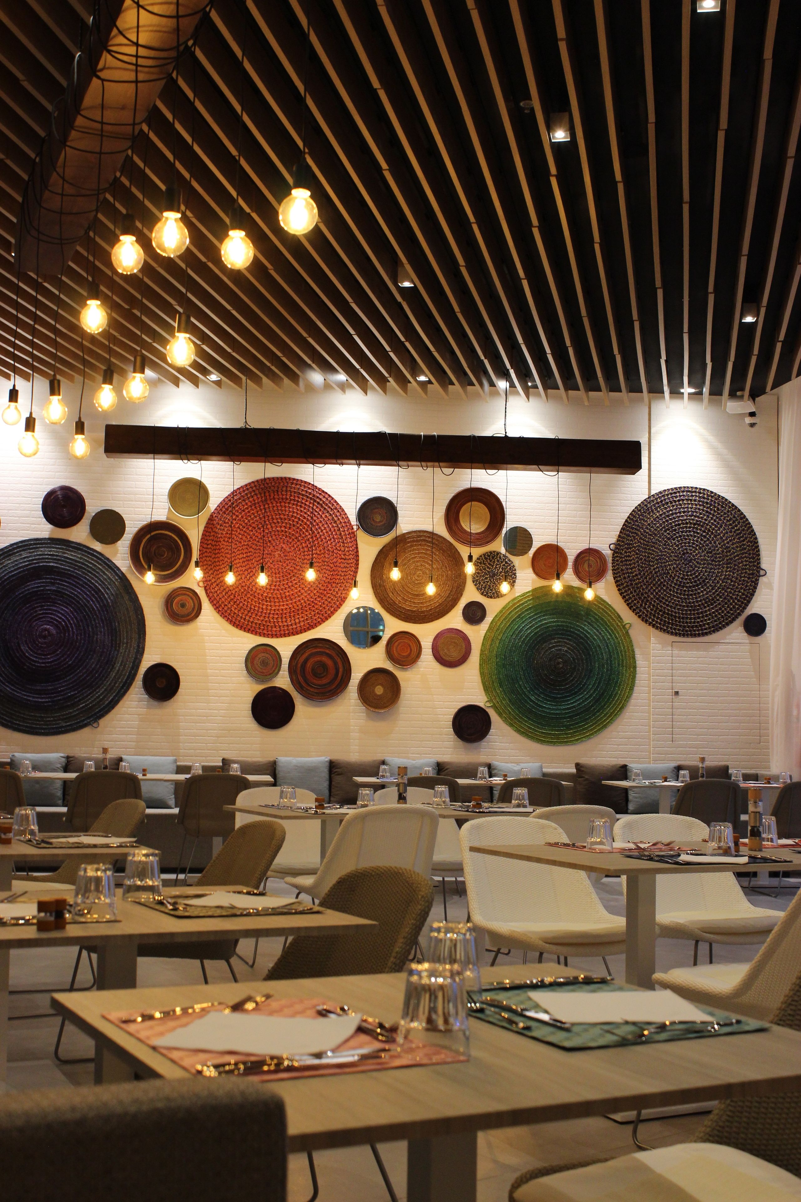 Uma sala de jantar moderna com mesas postas para refeições, iluminação suspensa e obras de arte decorativas na parede.