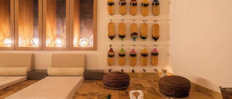 A spa room with a massage table, two bean bags, and a wall of wooden bottles.