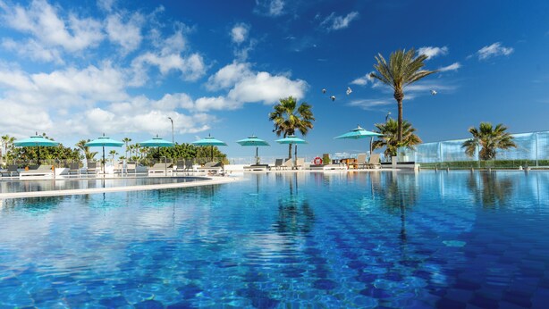 A clear blue pool with lounge chairs and umbrellas, surrounded by palm trees and a clear sky. - Sousse Pearl Marriott Resort & Spa (Sousse)