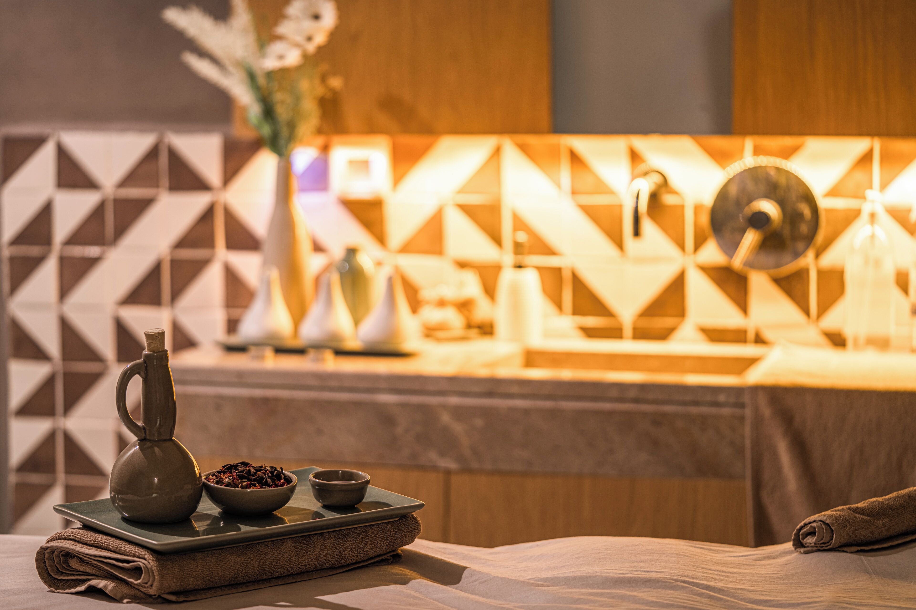 A neatly arranged spa area with a towel, a tray with a bowl of nuts, a small pitcher, and a decorative vase.