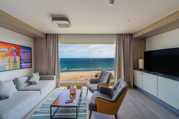 A modern living room with a large TV, comfortable seating, a coffee table, and a view of the beach. - Sousse Pearl Marriott Resort & Spa (Sousse)