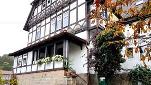 Un edificio tradicional con entramado de madera, base de piedra, puerta verde y macetas con flores en los alféizares de las ventanas.
