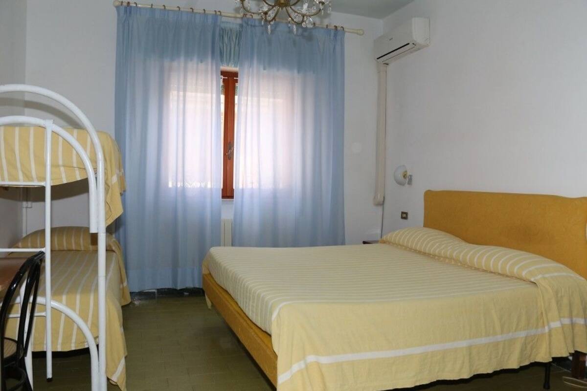 Une chambre avec un lit simple, un lit superposé, une chaise et une fenêtre avec des rideaux.
