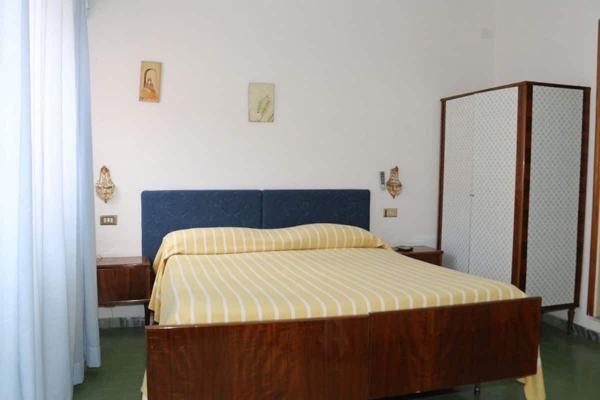 Une chambre à coucher avec un lit en bois, une tête de lit bleue, une table de chevet, une commode, une armoire et deux lampes fixées au mur.