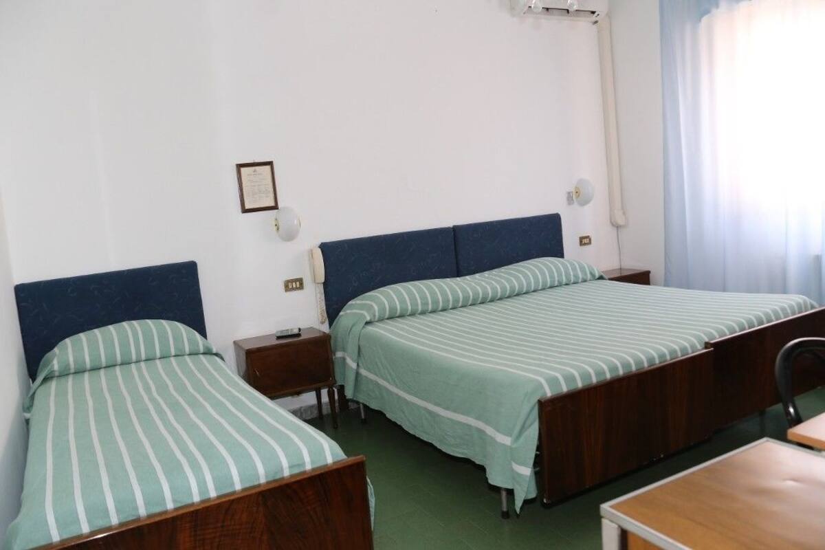 Une chambre avec deux lits simples, chacun doté d’une tête de lit en bois et d’une literie à rayures vertes. La chambre comprend également un bureau et une chaise en bois.