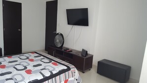 A bedroom with a bed, a TV mounted on the wall, a fan, and a small cabinet. - Apartamento Superior Laguito (Cartagena)