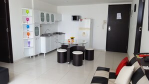 A modern kitchen with white cabinets, a glass-top dining table, and black stools. - Apartamento Superior Laguito (Cartagena)