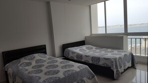 A room with two beds, a large window with a view of the sea, and a balcony. - Apartamento Superior Laguito (Cartagena)