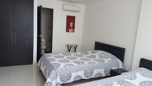 A bedroom with a bed, a wardrobe, a small table, and a toilet visible through an open door. - Apartamento Superior Laguito (Cartagena)