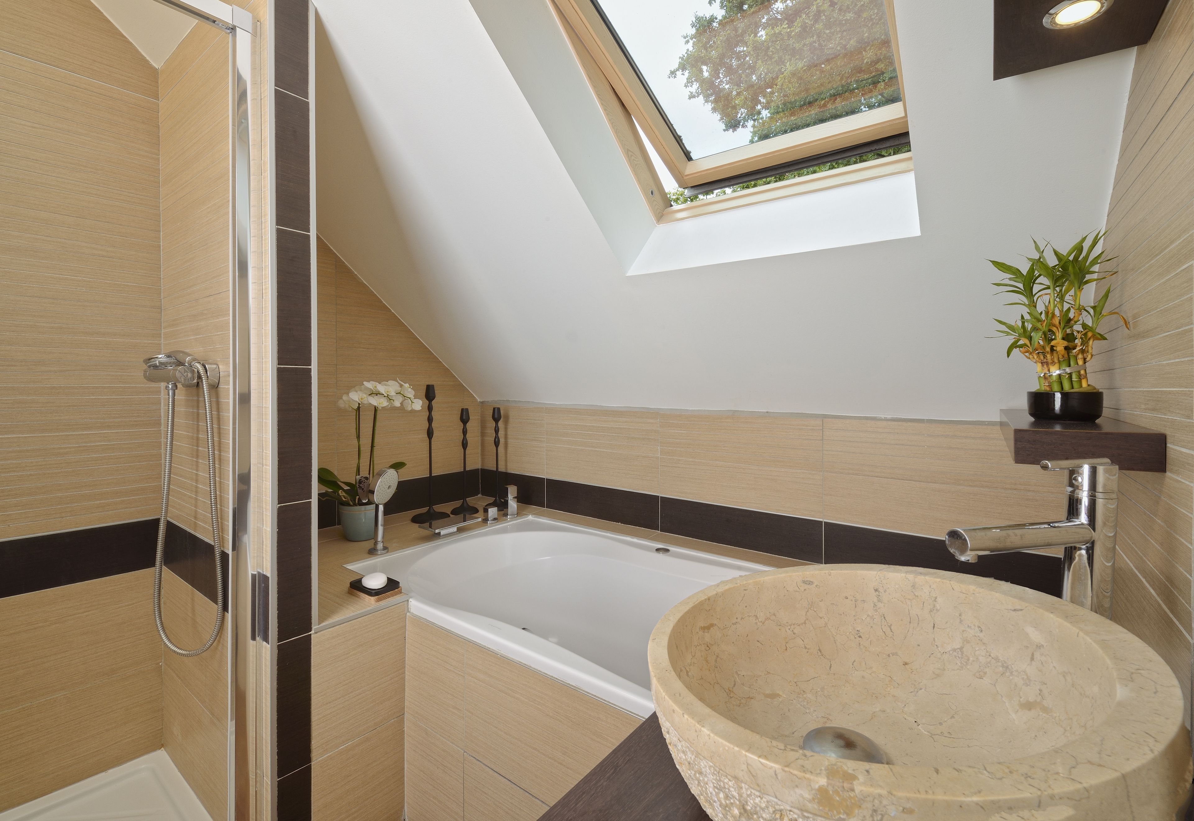 A modern bathroom with a skylight, a freestanding bathtub, and a large stone sink.