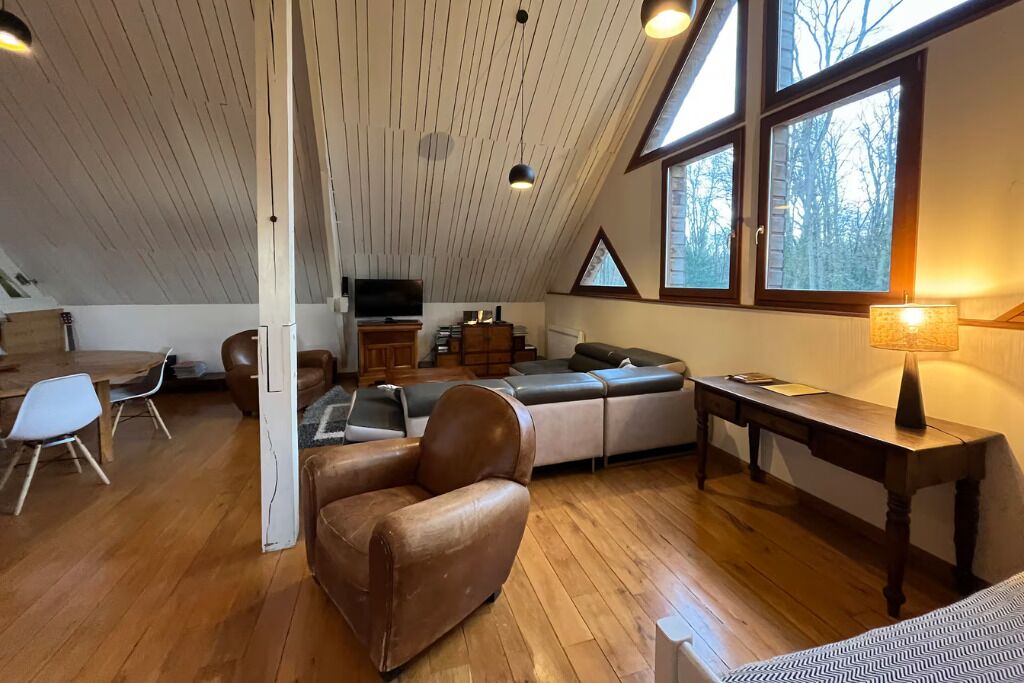 A loft-style room with a wooden ceiling, a sofa, a chair, a table, and a TV.