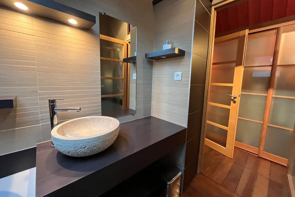 Un bagno moderno con una vasca in pietra, uno specchio e una porta in legno.