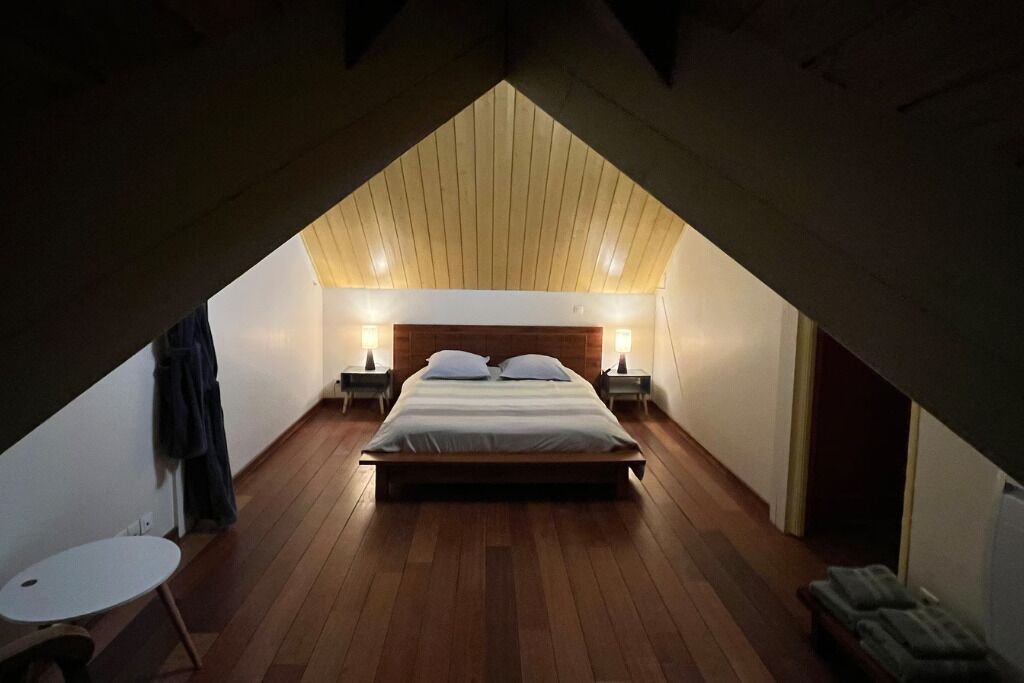 A bedroom with a sloped ceiling, a bed with pillows, two bedside tables with lamps, and a small round table.
