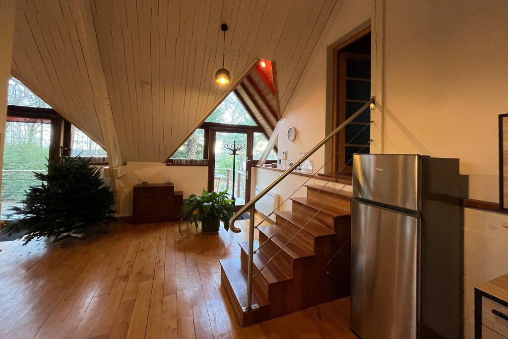 A wooden interior with a staircase, a refrigerator, and a Christmas tree.