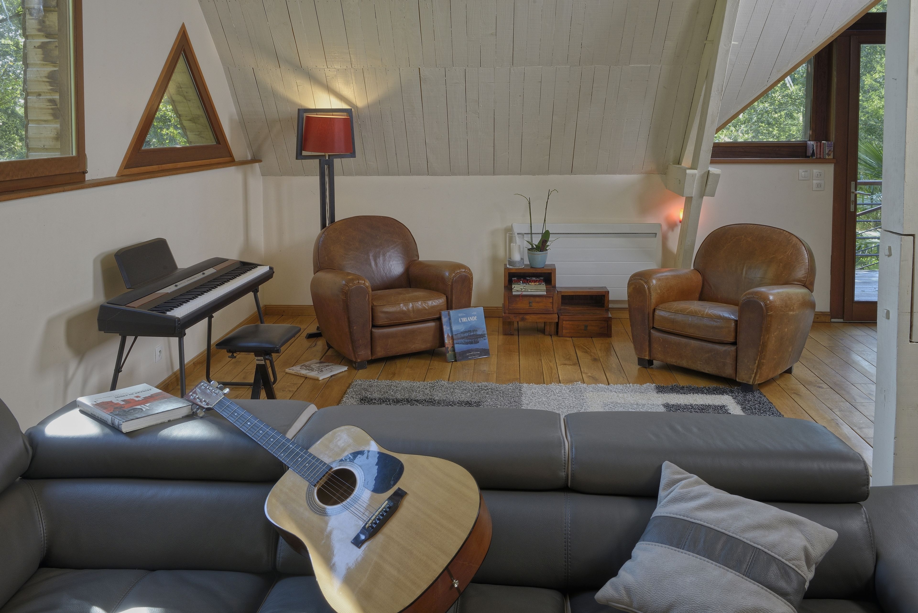 Un salon chaleureux avec un piano, deux fauteuils en cuir, un canapé et une guitare.