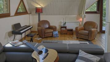 Un salon chaleureux avec un piano, deux fauteuils en cuir, un canapé et une guitare.