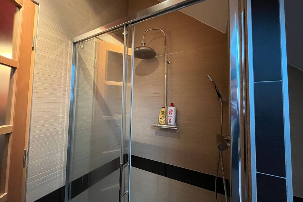 Un baño moderno con ducha acristalada, cabezal de ducha manual y toallero de pared.