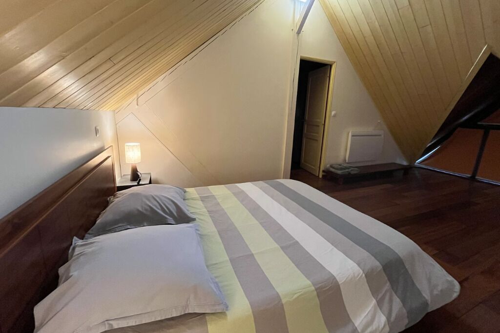 A bedroom with a sloped ceiling, a bed with striped bedding, a nightstand with a lamp, and a door leading to another room.