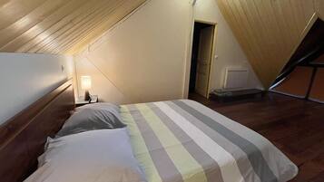 A bedroom with a sloped ceiling, a bed with striped bedding, a nightstand with a lamp, and a door leading to another room.