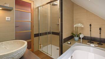 A modern bathroom with a glass-enclosed shower, a freestanding bathtub, a large stone basin, and a potted orchid.