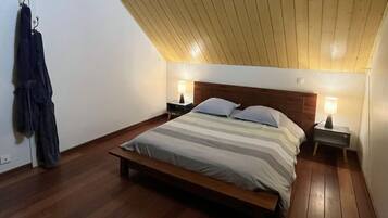Een slaapkamer met een houten bed, twee nachtkastjes met lampen, een schuine plafond en een jas aan de muur.