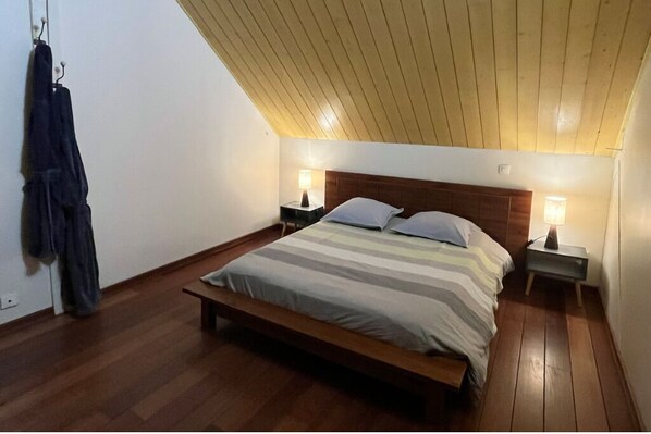 A bedroom with a wooden bed, two bedside tables with lamps, a sloped ceiling, and a coat hanging on the wall. - Loft d’architecte chaleureux et spacieux (Rives-du-Loir-en-Anjou)