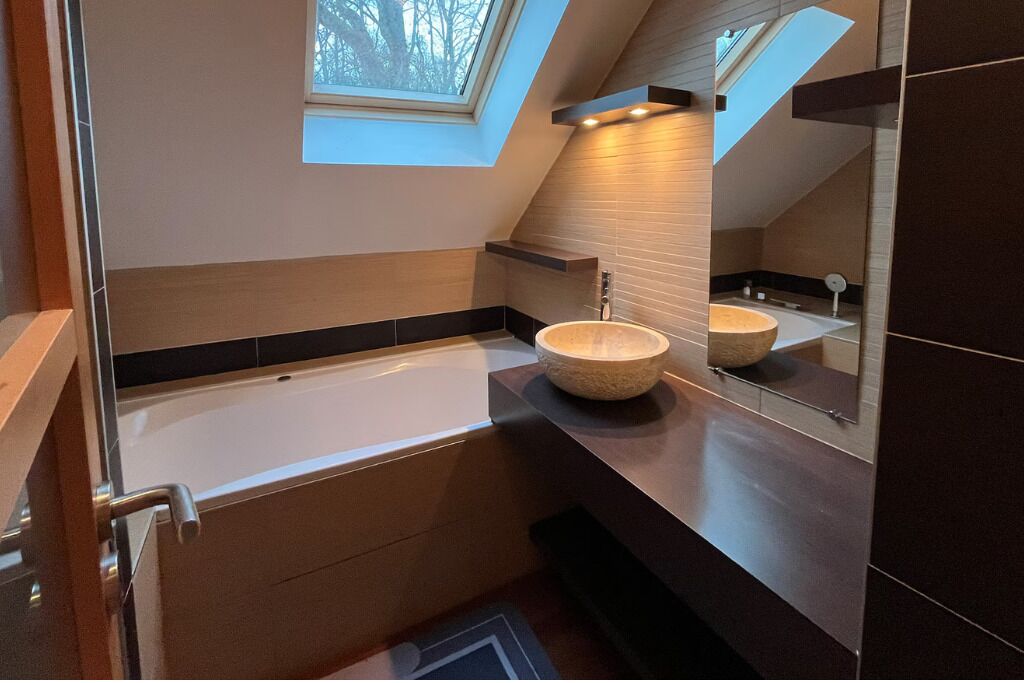 Un bagno moderno con finestra a lucernario, una vasca freestanding e uno specchio grande.