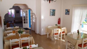 A dining area with multiple tables and chairs, a glass partition, and a view of an outdoor balcony. - Avra Hotel (Santorini)