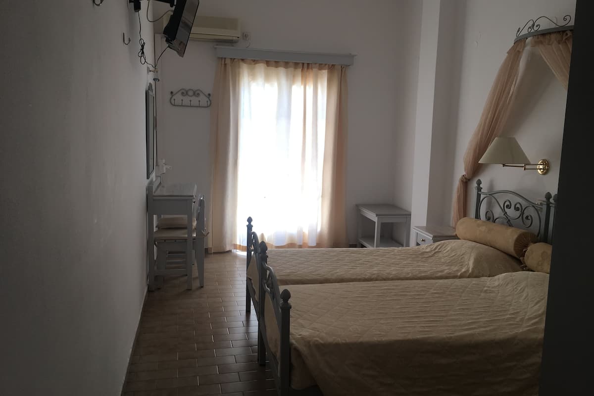 A bedroom with two beds, a desk, a chair, a small table, and a window with curtains.