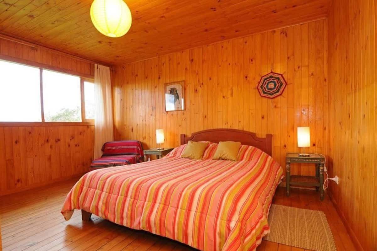 A wooden-paneled room with a large bed, two bedside lamps, a window, and a wall decoration.