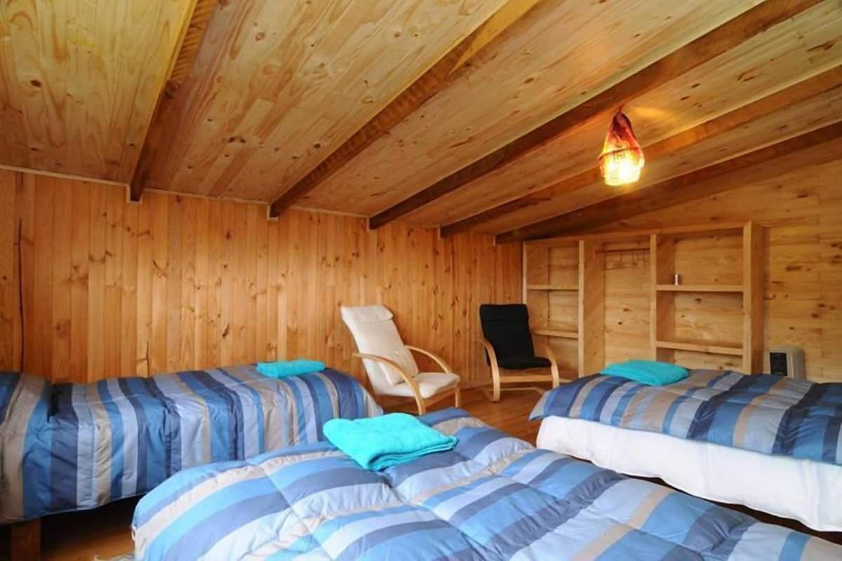 A wooden cabin room with two beds, a chair, and a shelf.
