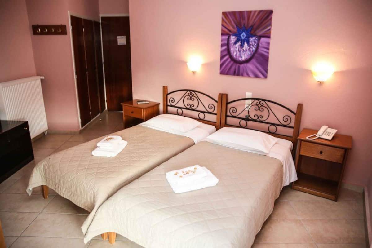 A double room with two beds, bedside tables, a wall-mounted phone, and a painting.