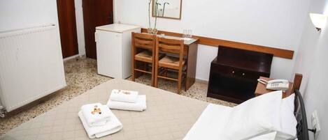 Habitación de hotel con cama, escritorio, silla, refrigerador pequeño y teléfono junto a la cama.