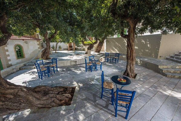 Un patio al aire libre con suelo de piedra, sillas azules y una mesa redonda.