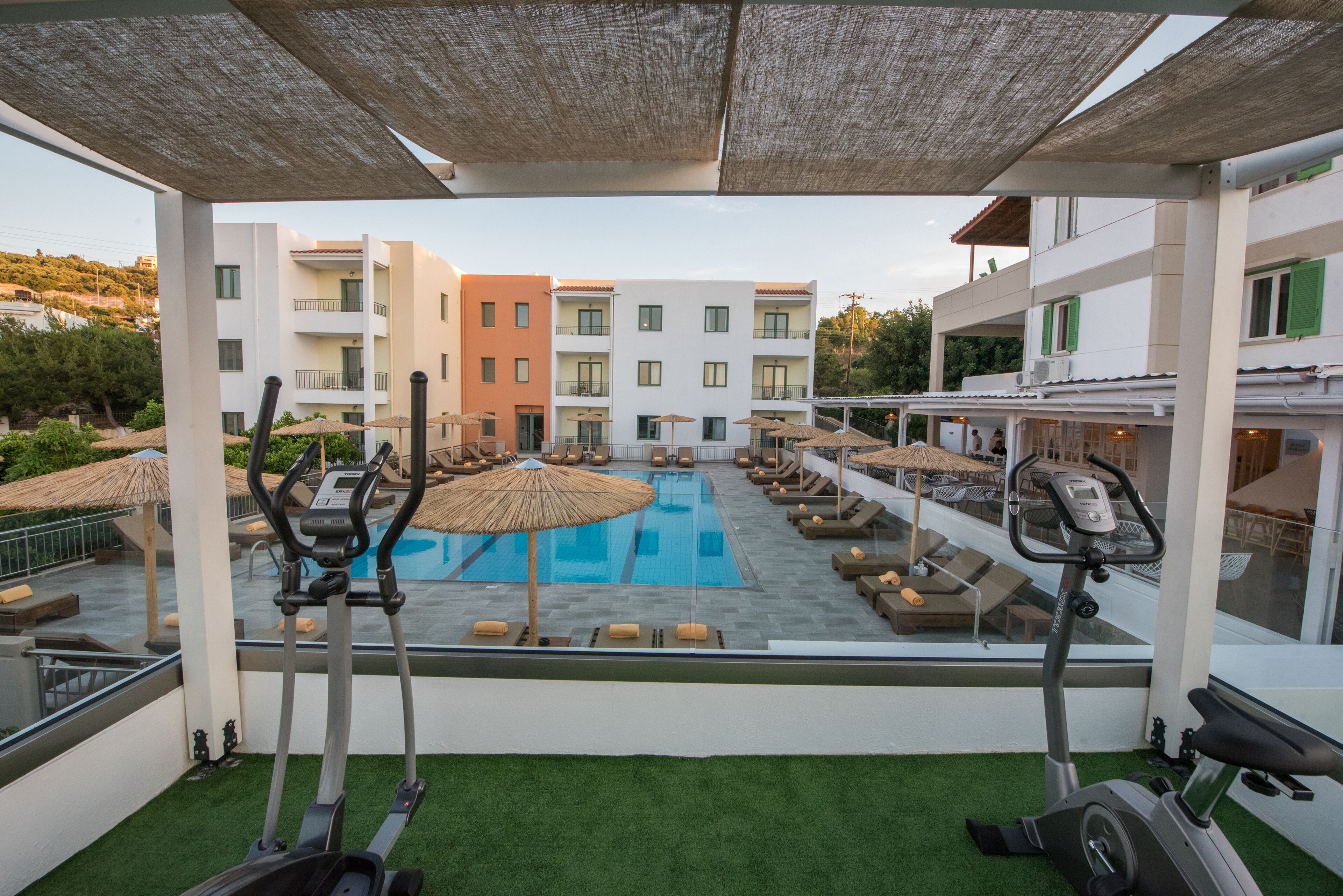 A rooftop pool area with exercise equipment, lounge chairs, and umbrellas.