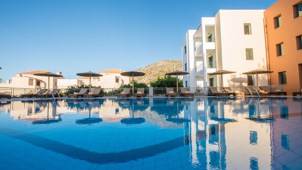 Una piscina con sillones de descanso y sombrillas, rodeada de edificios con balcones y una montaña al fondo.