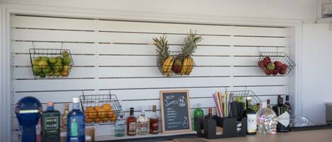 A bar area with a chalkboard menu listing fresh juices, a selection of fruits, and various bottles of alcohol.