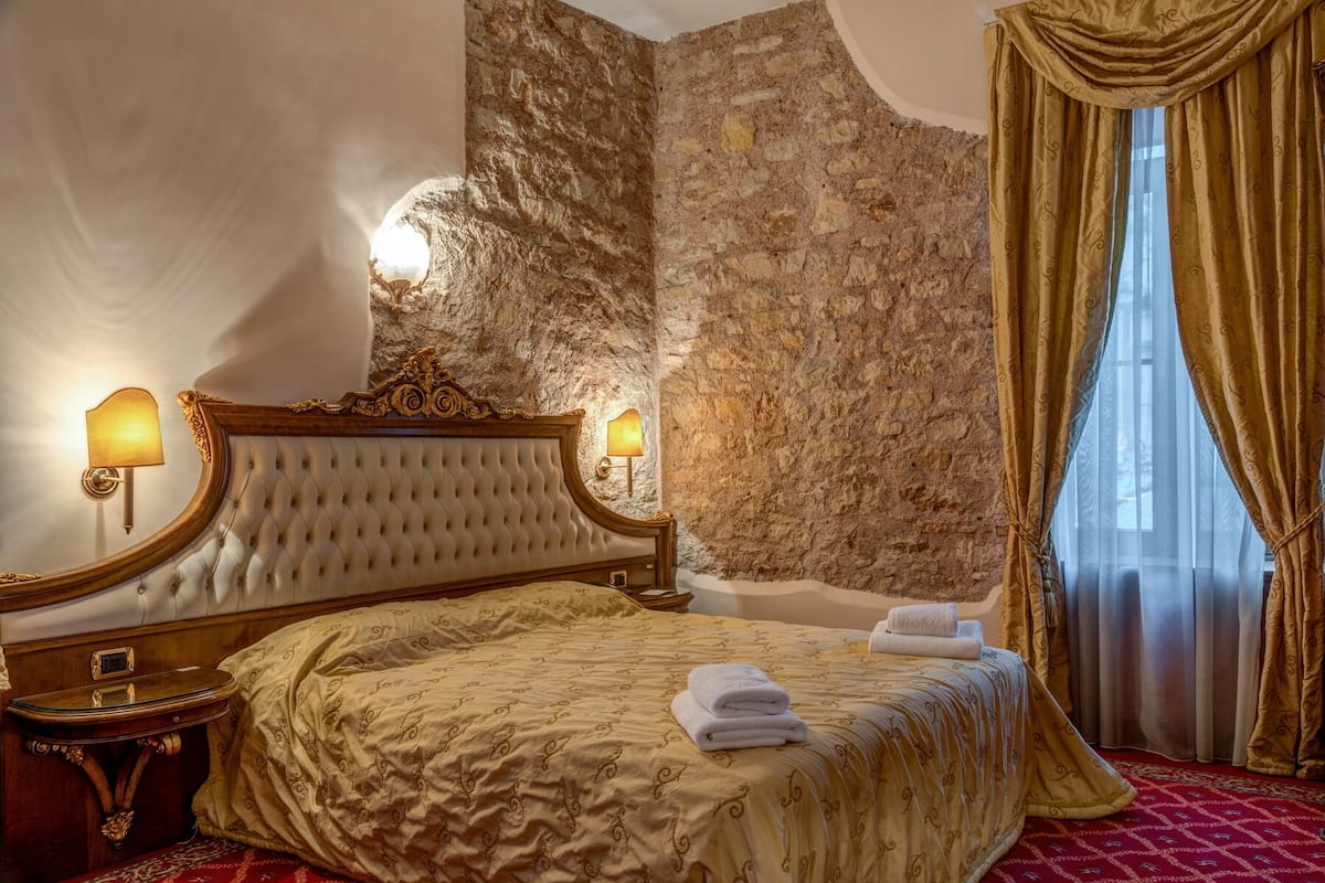 A luxurious bedroom with a large bed, ornate headboard, and a stone wall.