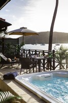 Un área de piscina con vista a barcos en el agua, una mesa con sillas y una tumbona.