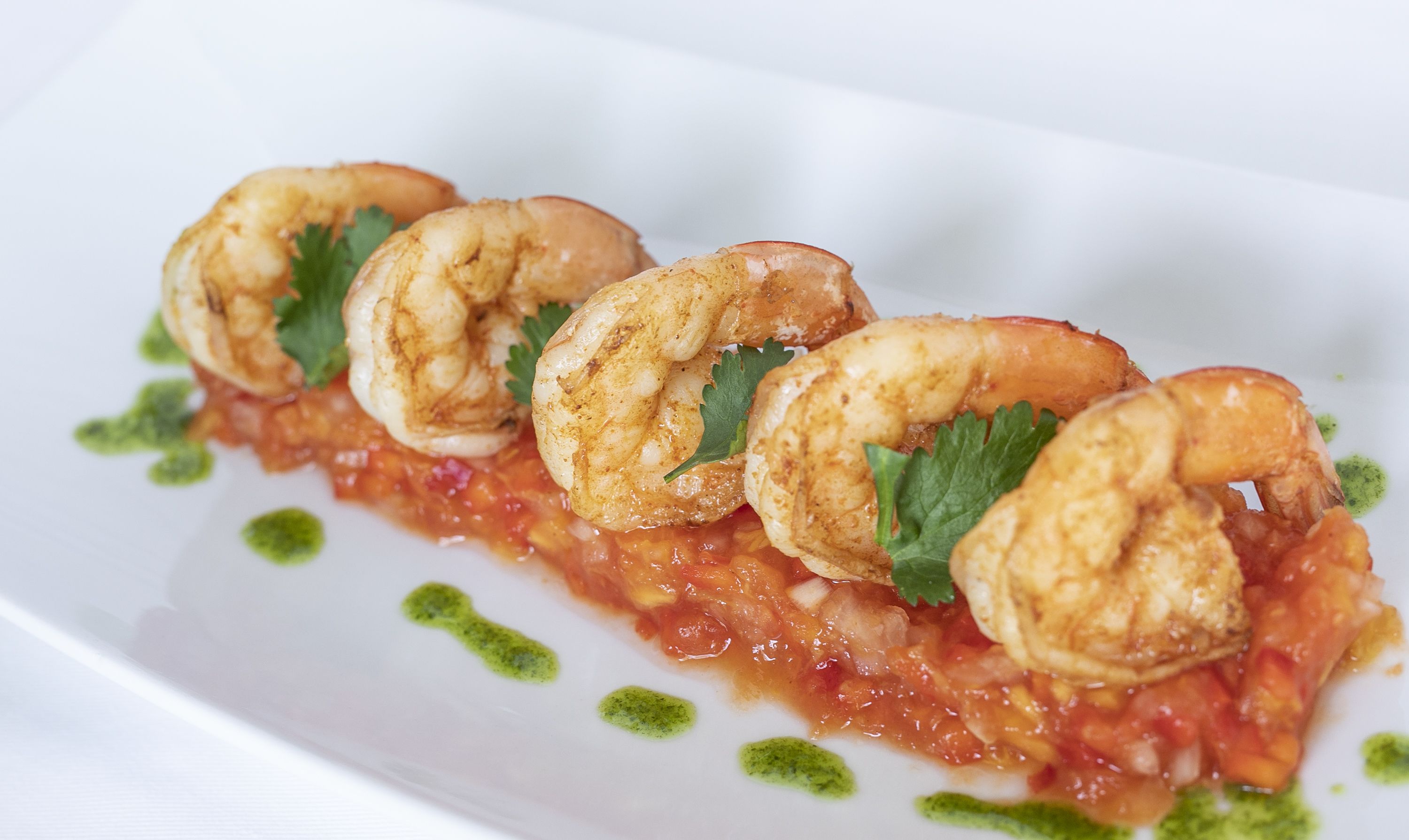 Une assiette de crevettes, garnie d’une sauce verte.