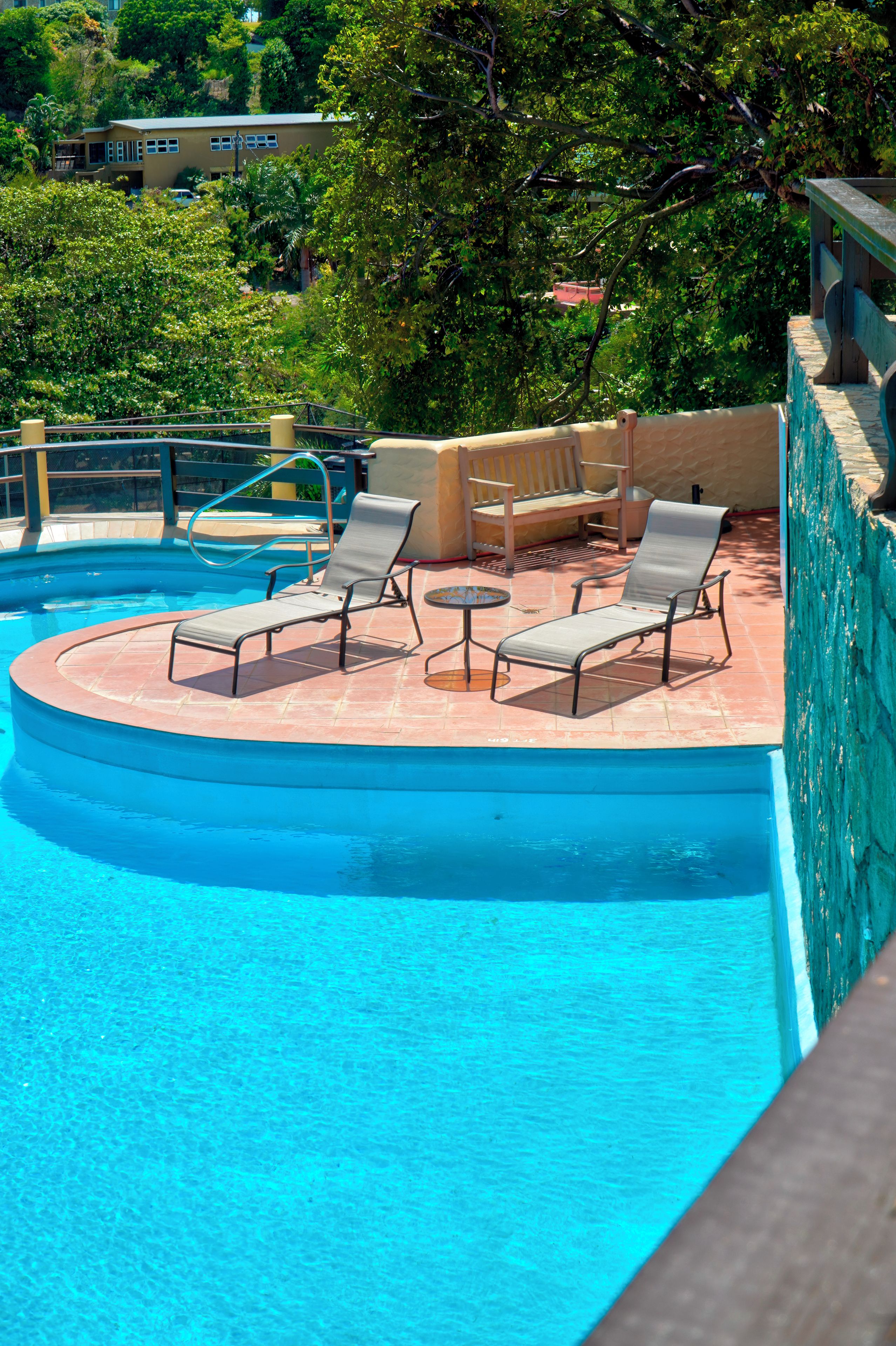 A pool area with lounge chairs and a small table, surrounded by a stone wall and greenery.