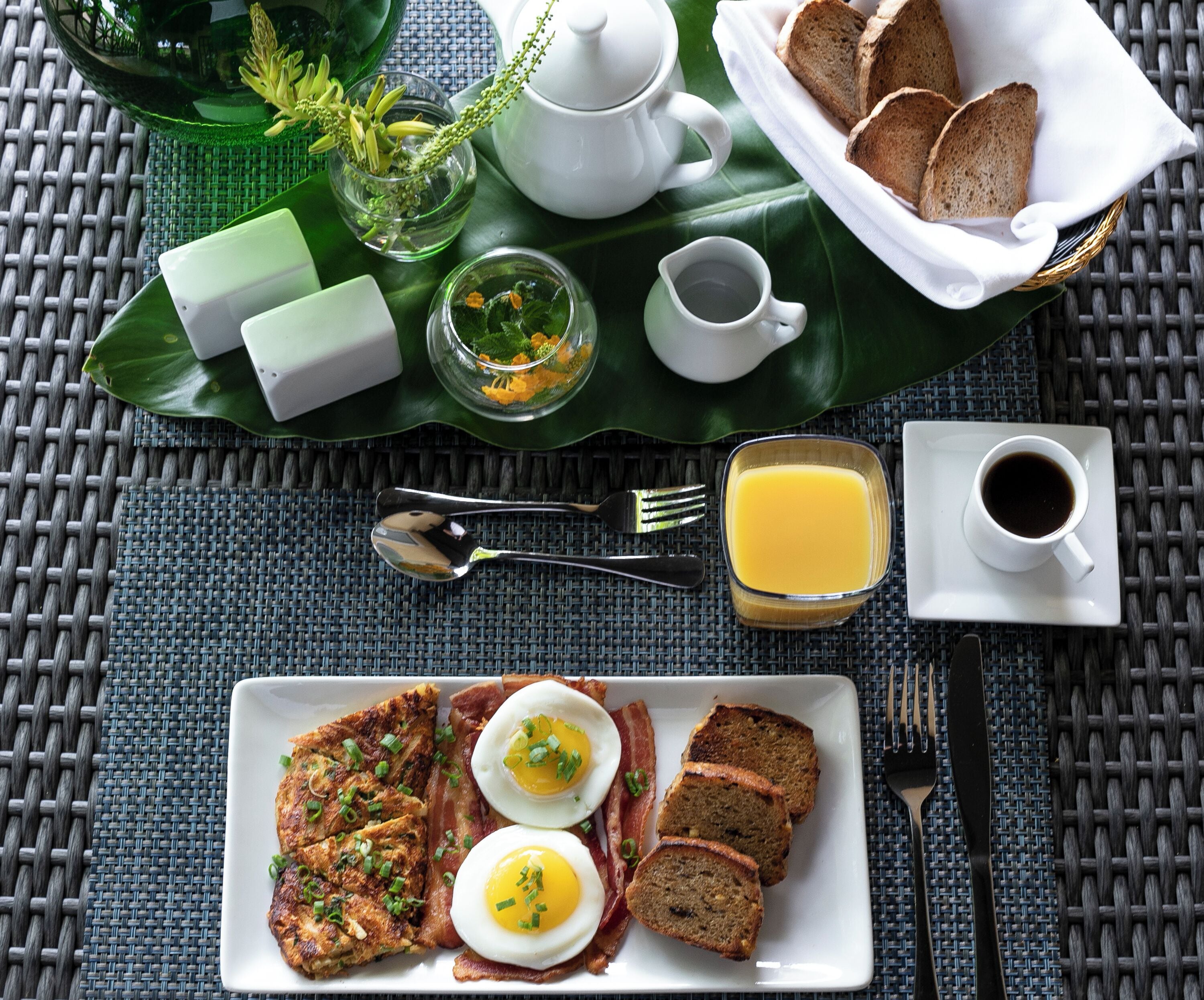 A breakfast tray with toast, eggs, bacon, and juice on a woven tablecloth.