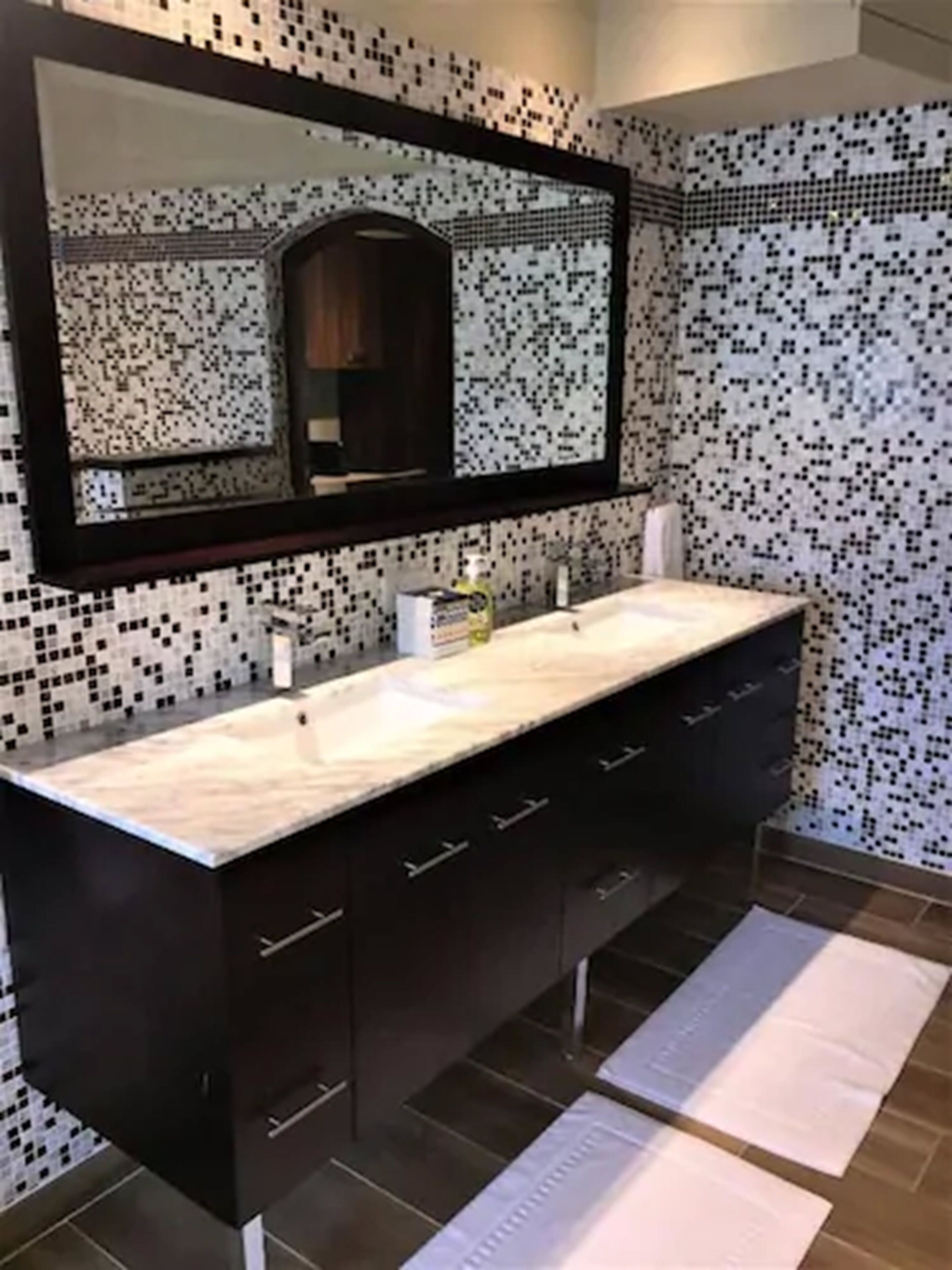 A modern bathroom with a large mirror, dark cabinetry, and a tiled backsplash.