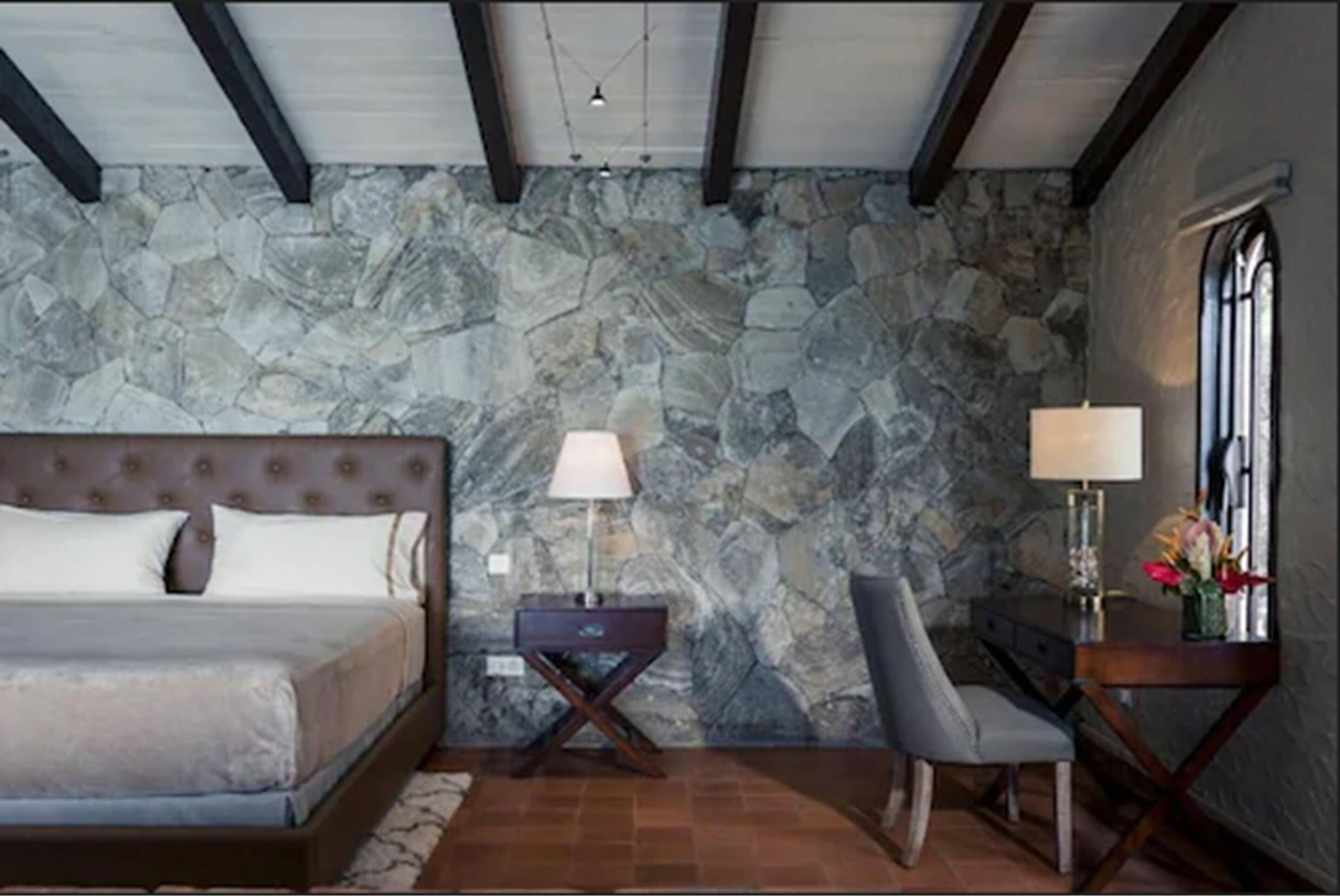 Un dormitorio con pared de piedra, una cama, un escritorio y una silla.