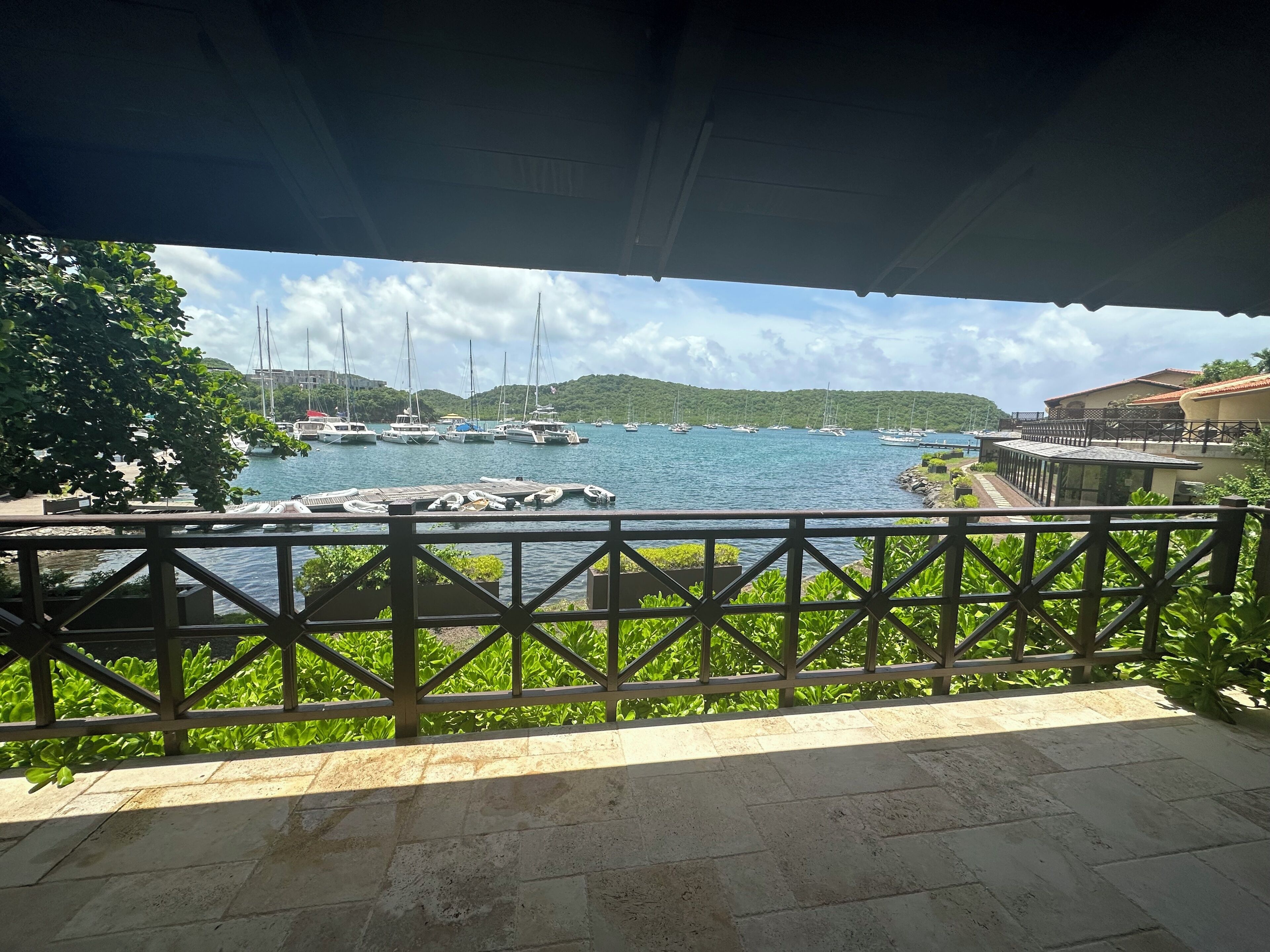 Une vue d’une marina avec des bateaux amarrés, une zone abritée avec une rambarde et de la végétation au premier plan.