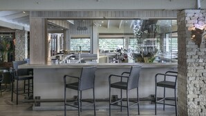 Una zona de bar con pared de piedra, sillas de mimbre y vistas al exterior.