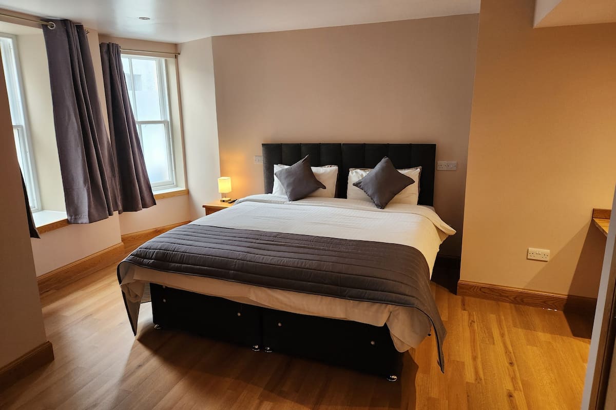 A bedroom with a bed, curtains, a nightstand, and a window.