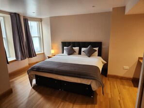 Une chambre à coucher avec un lit, des rideaux, une table de chevet et une fenêtre.